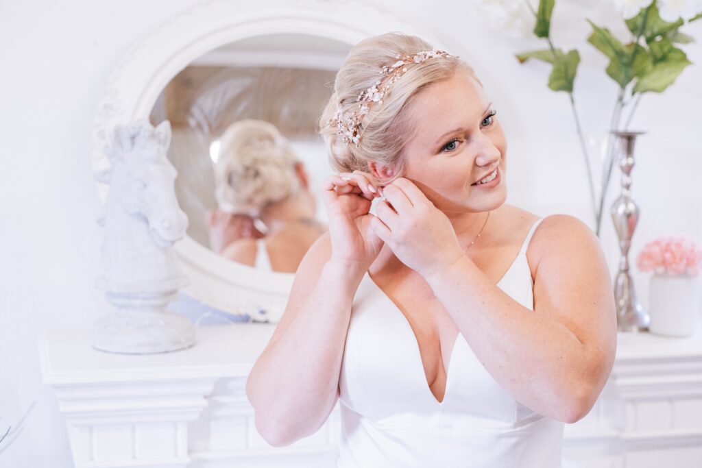 A woman putting on her earrings in front of a mirror.