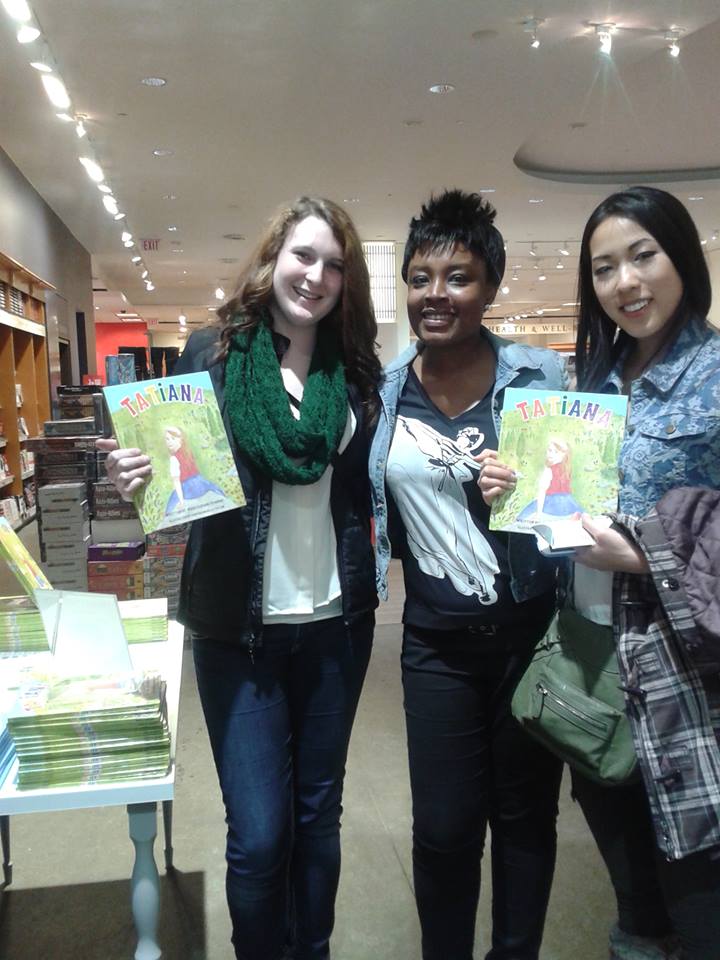 Three women holding up books in a store.